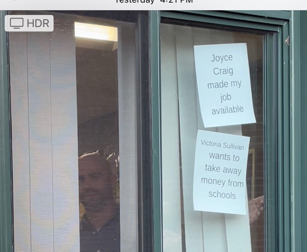 Teacher with signs in McLaughlin window