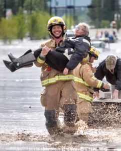 grinning firefighter carrying old lady out of a flood CBC.CA